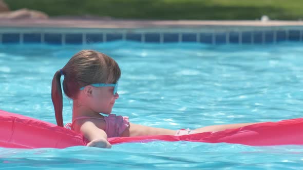 Young Joyful Child Girl Having Fun Swimming on Inflatable Air Mattress in Swimming Pool with Blue