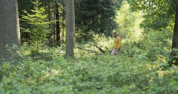 A Young Man Wearing a Yellow Jacket with a Hat That Has a Safety Net is Heading Through the Woods