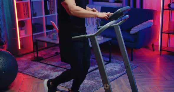 Asian Guy in Sportswear Pressing Buttons on Treadmill's Control Panel and Starting to Run