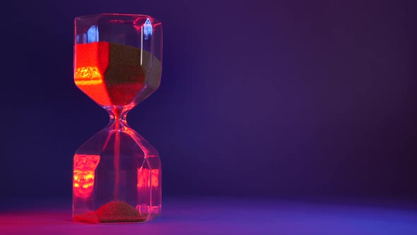 Glass Hourglass with Golden Sand on Purple Background