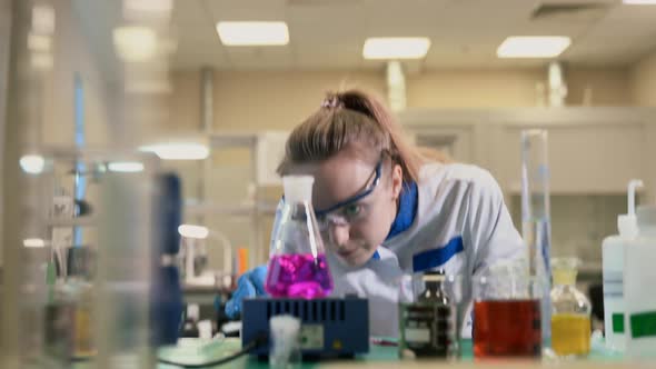 Scientist Observing Pink Liquid Bubbling in Lab Flask