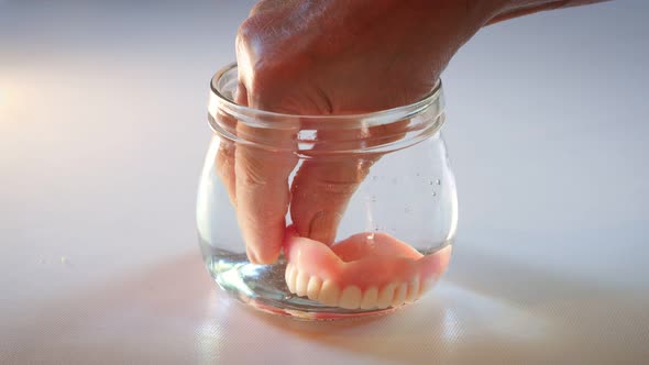 Hand taking artificial teeth out of glass of water.