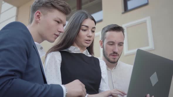 Portrait Cute Young Woman and Two Men in Formal Wear Discussing Project on the Laptop on the Terrace