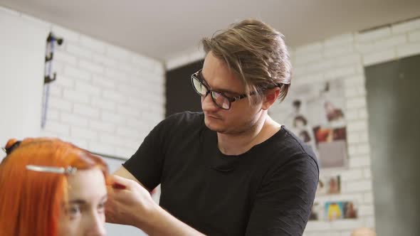 Stylish Male Hairdresser in Glasses is Cutting Redhead Woman's Hair in Beauty Salon