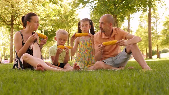 A Happy Family Enjoys a Picnic in the Park They Eat Corn Together and Smile