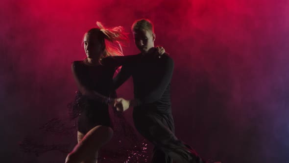 Young Couple Cheerfully Dancing Jive on a Smoky Background with Crimson Backlight. Slow Motion