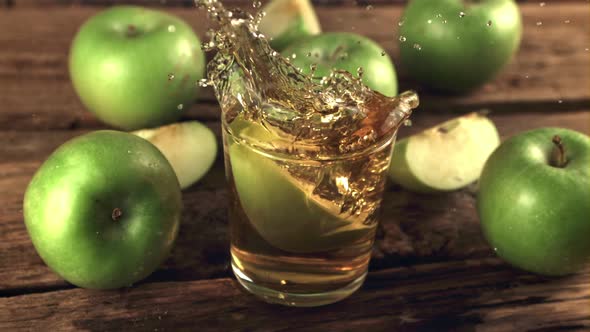 Super Slow Motion a Piece of Green Apple with Splashes Falls Into a Glass of Juice