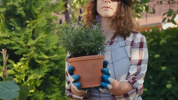 Young Female Gardener Sniffs Lavender Plant in Pot Outdoors