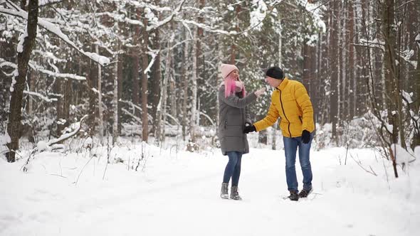 A Man in a Yellow Jacket and a Girl in a Hat and Scarf Walk Through the Winter Forest During a