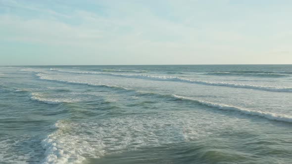 Surfer in Ocean with White Foam Waves in Afternoon Light and Clear Sky, Aerial High Angle Forward