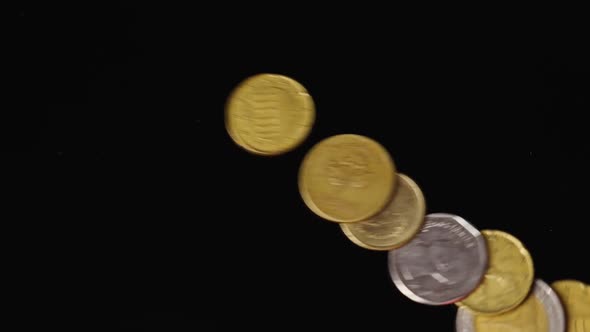 Coins from different countries fall on a black mirror background in slow motion