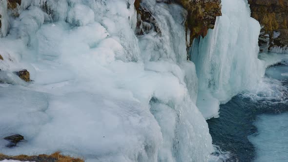 Closeup of Frozen Waterfall Bottom with Icy Rocks and Flowing Down Water