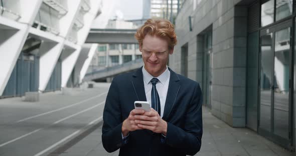 Redheaded Smiling Businessman in Eyeglasses and Formal Suit Stand in the City Center Street Uses