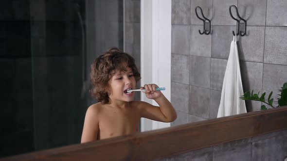 Small Boy with Brown Curly Hair Uses Toothpaste and Toothbrush while Brushing Teeth Before