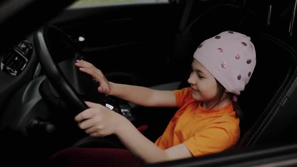 Happy Little Girl is Sitting Behind the Wheel of the Car