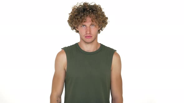 Fairhaired Curly Male Model Posing on Camera Showing Thumb Down Dislike Blowing Off Hair From