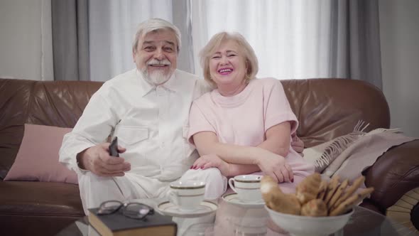 Portrait of Positive Mature Caucasian Couple in Love Watching TV in the Evening. Happy Senior