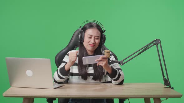 Upset Asian Woman Gamer With Headphone Losing Mobile Phone Game On The Green Screen Background