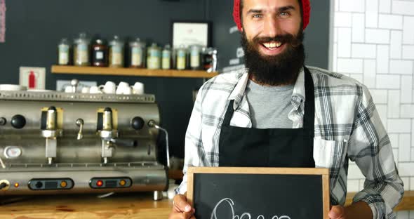 Portrait of waiter standing with open sign board