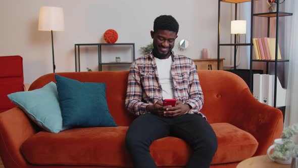 Cheerful Young Man Sitting on Sofa Using Mobile Phone Share Messages on Social Media Application