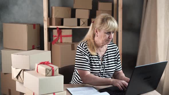Mature Saleswoman Using Computer While Checking Orders in Ecommerce Clothing Store
