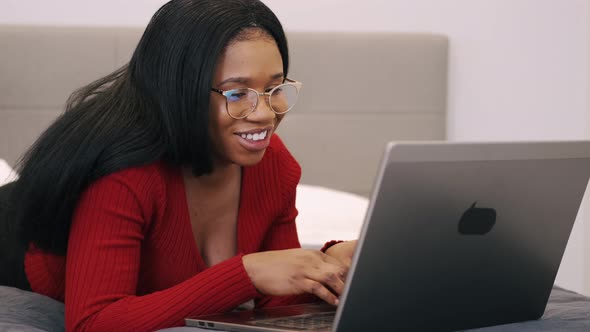 Young Afrrican American Woman Laying on Bed with a Computer