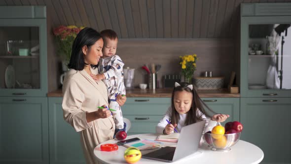 Cheerful Asian mother doing homework with her daughter and son on her hands