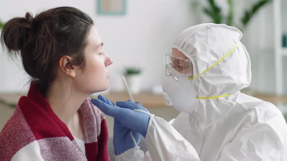 Doctor in Protective Uniform Collecting Nasal Swab from Female Patient at Home