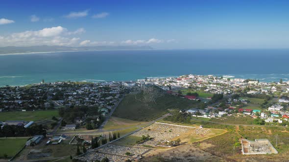 Panning shot of coastal town next to bay, aerial view from mountain, Hermanus, South Africa.