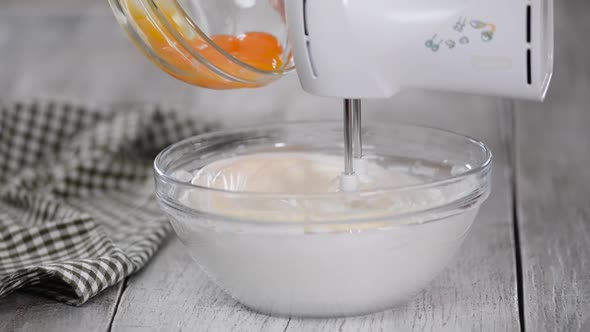 Adding Raw Egg Yolks To Creamy White Batter in Mixing Bowl.