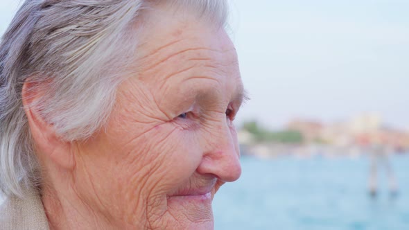 Elderly Woman Traveler Stands By Waterside Enjoying View