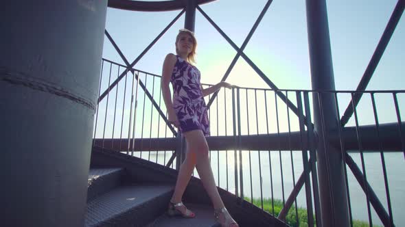 Blonde Girl Stops on a Tower in Front of the Sea