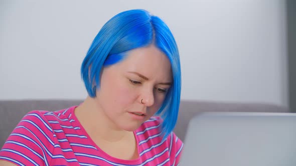 Young white girl with blue hair learning online with modern laptop computer and fast internet