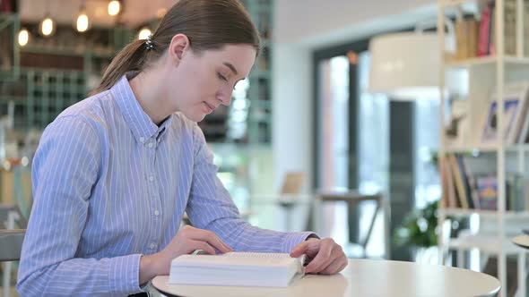 Focused Young Businesswoman Reading Book in Cafe