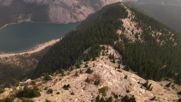 Aerial 4K footage of a drone flying over a mountain with lot of pine trees and  big blue lake at the