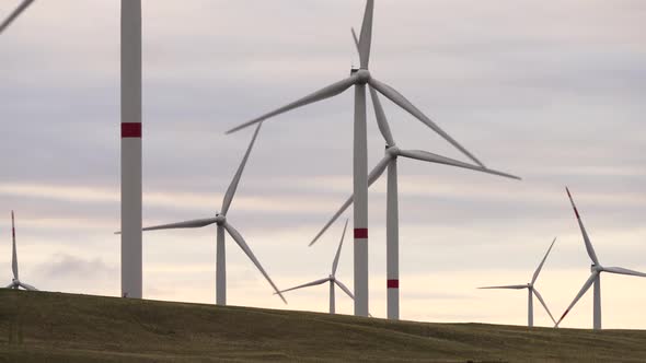 Motion the Blades of a Large Wind Turbine in a Field Against a Background of Orange Sunset on the