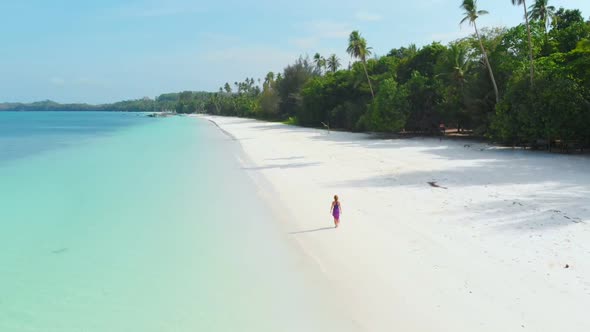 Aerial Slow motion: woman walking on white sand beach turquoise water tropical coastline alt