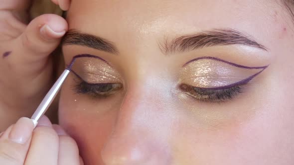 Girl Stylist Makeup Makeup Artist Applies a Thin Line of Purple Eyeliner on Shiny Makeups in Gold