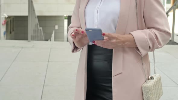 Elegant Businesswoman Typing a Text Letter on a Mobile Phone Using the Internet