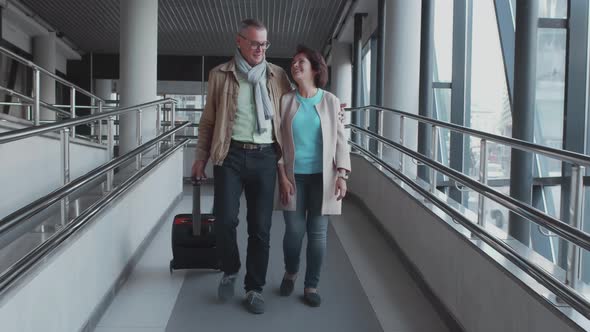 Beautiful Senior Couple Walking in the Hallway of Airport with Luggage and Hugging