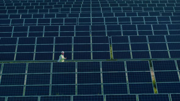 Aerial View of Engineer Examining Solar Panels on Field