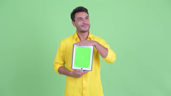 Happy Young Hispanic Businessman Thinking While Showing Digital Tablet