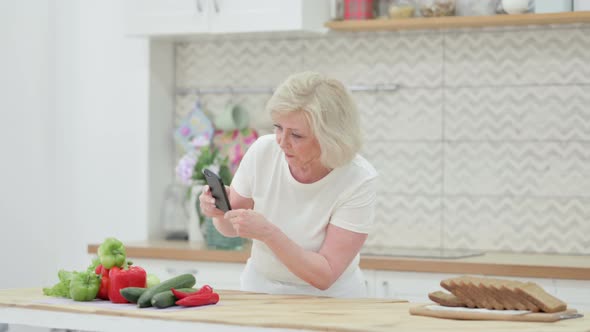 Attractive Senior Old Woman Making Online Payment on Smartphone in Kitchen