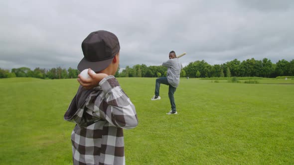 Closeup of African Son Pitching Baseball to Batting Father Outdoors