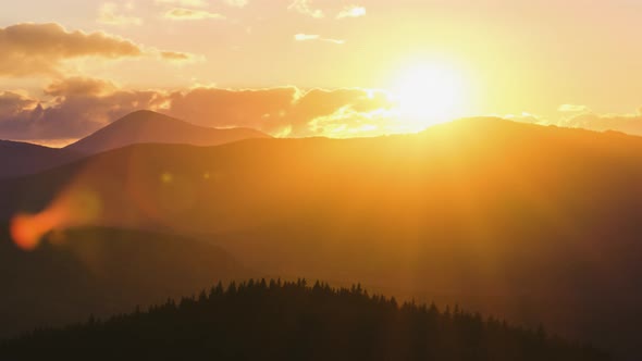 Beautiful Evening Panoramic Landscape with Bright Setting Sun Over Distant Mountain Peaks at Sunset