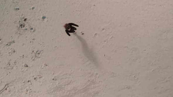 Aerial View Young Happy Woman (Wears Black Sweater and Leggings) Lays Down and Makes Sand Angel on