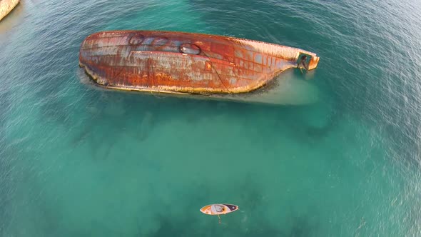 Aerial shot of young woman sup standup paddleboarding near a shipwreck in the Caribbean.