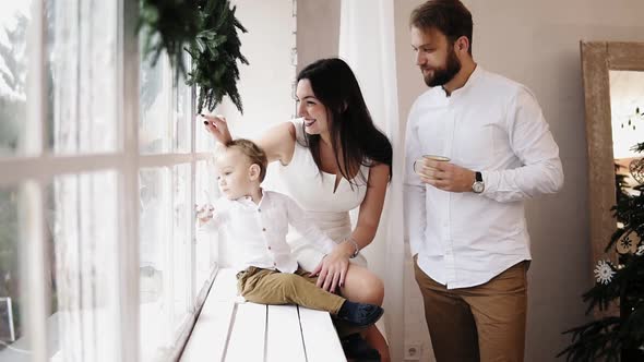 Young Lovely Family Sitting Together By the Window Decorated with Christmas Wreath