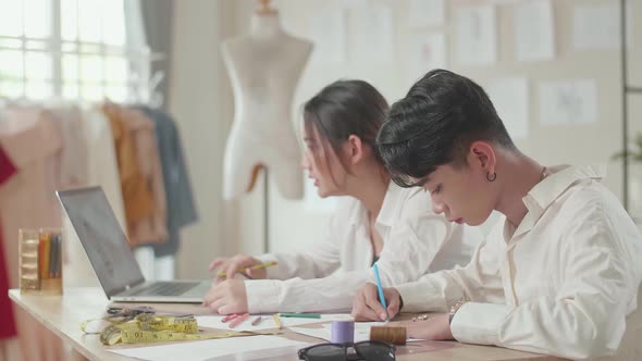 Two Fashion Designers Working With Laptop And Sketching At Fashion Design Studio