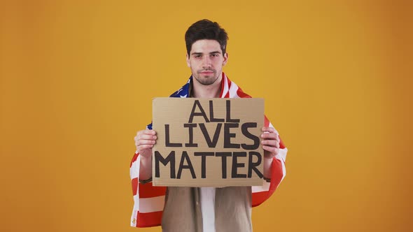 Young Guy Wrapped in Flag of USA is Raising Up Cardboard Tablet with Inscription All Lives Matter